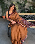Rajathee Saree Earthy Brown Cambric Silk Saree featuring a small peacock motif border and a soft, graceful sheen.