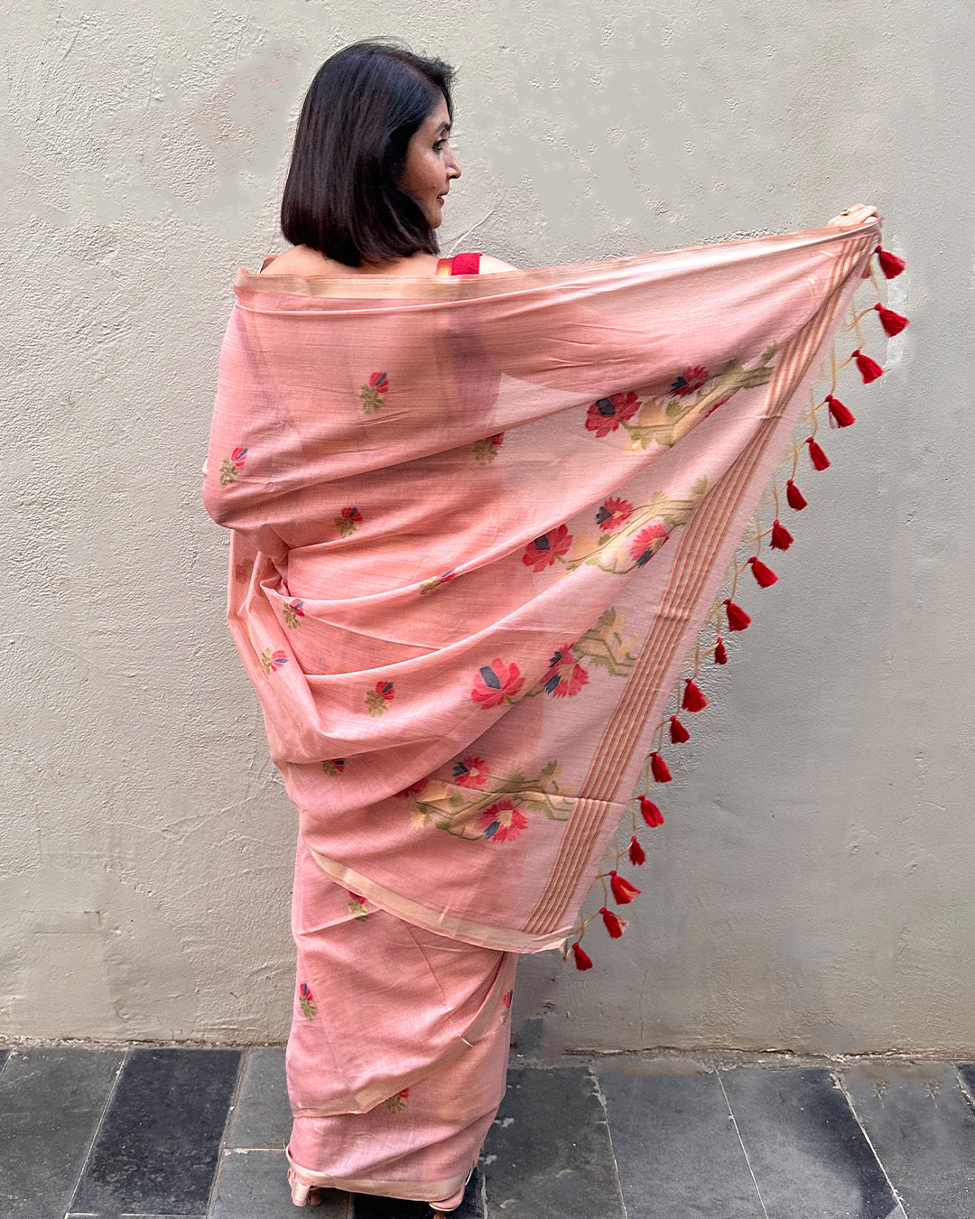 Back view of the Blush Pink Tussar Silk Saree showcasing the floral pallu design and vibrant red tassel detailing.