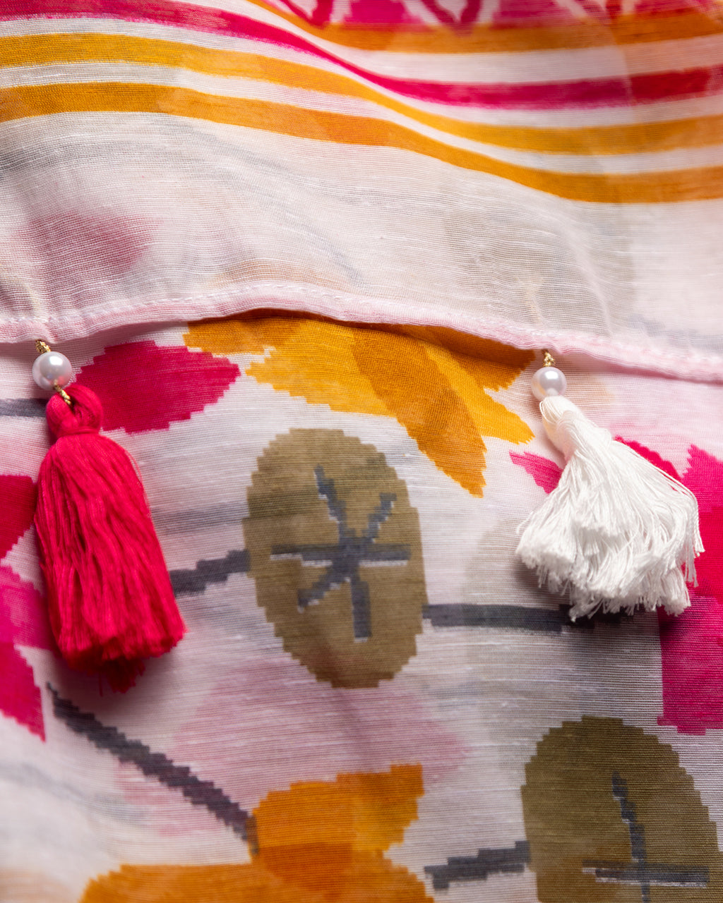 Close-up of the saree pallu showing intricate pink lotus motifs and vibrant tassels in pink and yellow.