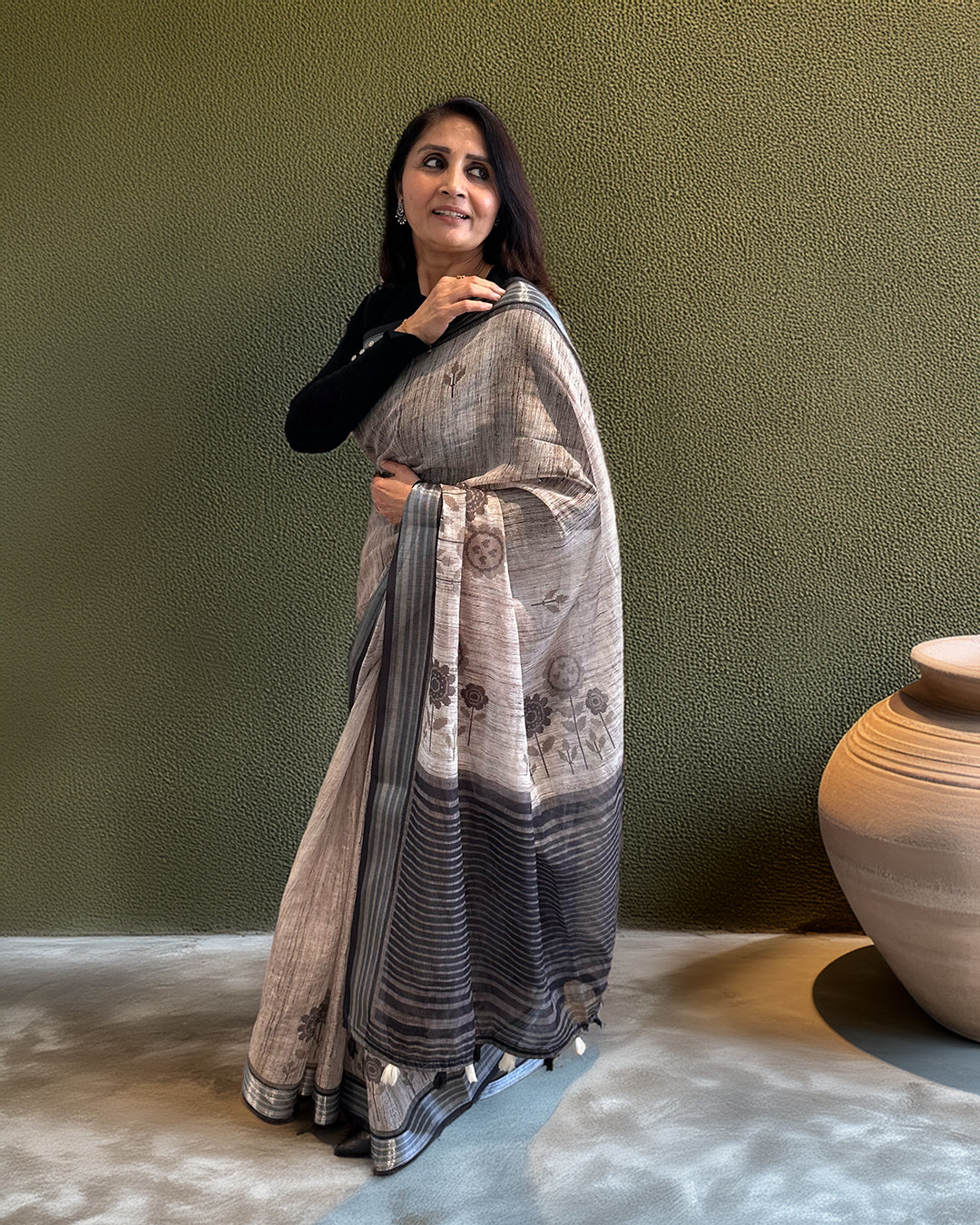 A model showcasing the lightweight and breathable drape of a charcoal brown cotton saree with contemporary floral accents.