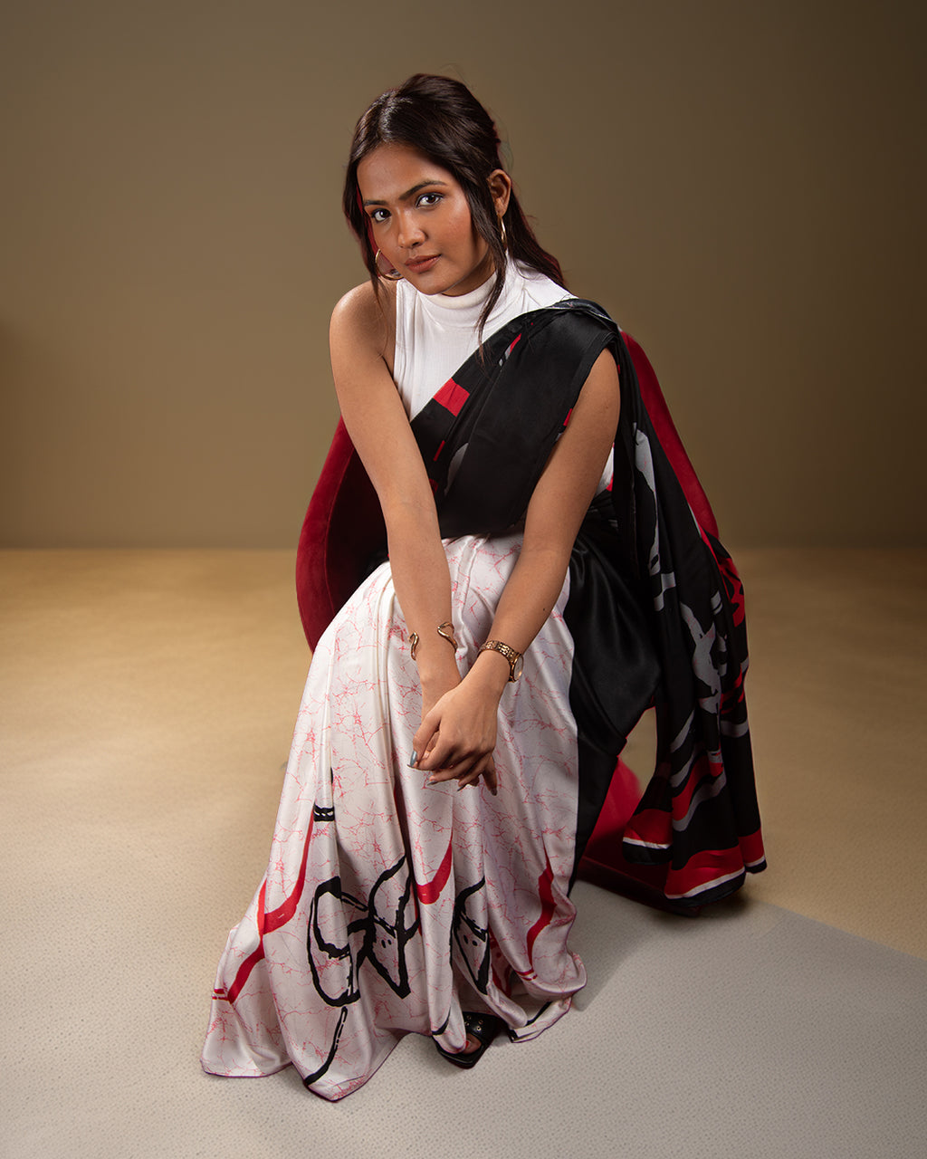 A model seated gracefully in a contemporary black and white crepe saree featuring bold red abstract brush strokes and a flowy silhouette.
