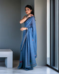 A model elegantly posing in a blue Mul cotton saree with a denim-inspired weave, featuring handcrafted thread and appliqué details for a contemporary, structured look.