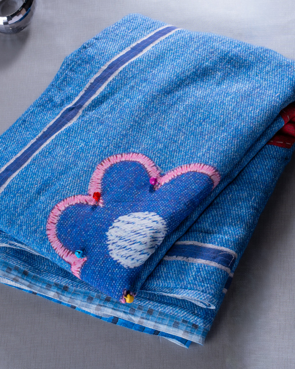 A close-up of the folded saree showcasing the intricate handcrafted pink floral thread work and denim-textured weave.