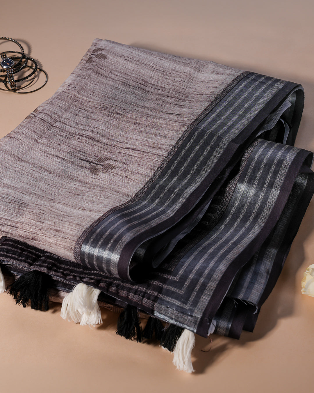 A neatly folded charcoal brown cotton saree displaying the fabric texture and the elegant striped border design.