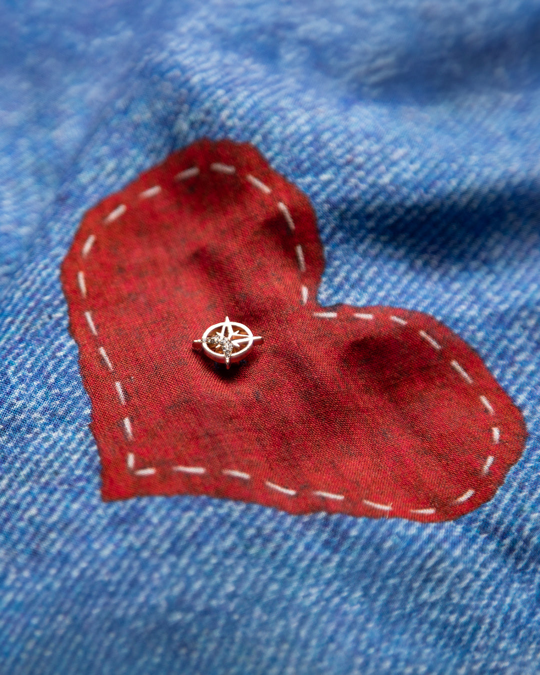 Macro shot of a unique handcrafted red heart appliqué with white contrast stitching on the blue denim-inspired cotton fabric.