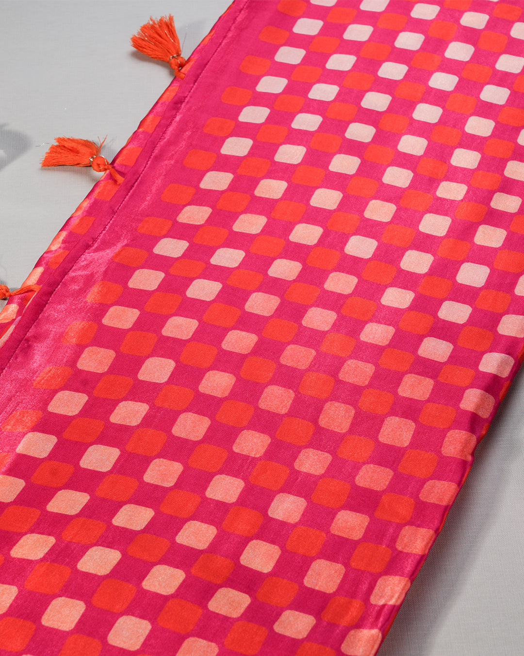 Detailed view of the checkered grid pallu and coordinating orange tassels on the Crimson Red Rajathee Saree.