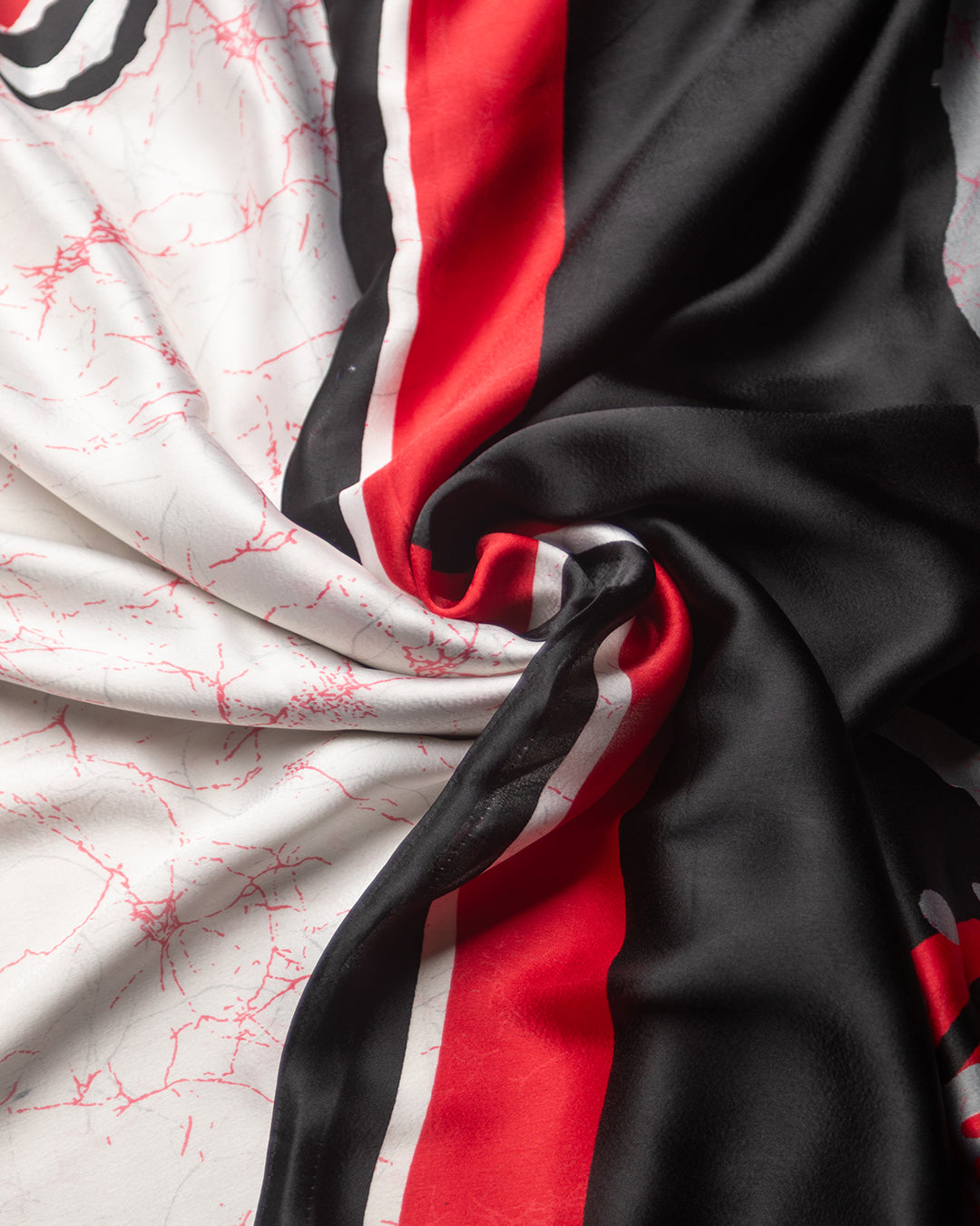 A detailed macro view of the artistic abstract brush spread print on white crepe fabric with red and black motifs.