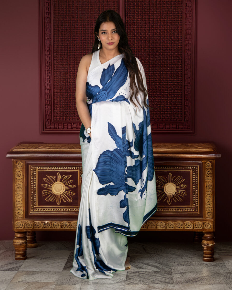 A model elegantly posed in a white crepe saree featuring a bold, large blue abstract floral print, highlighting its lightweight and flowy drape.